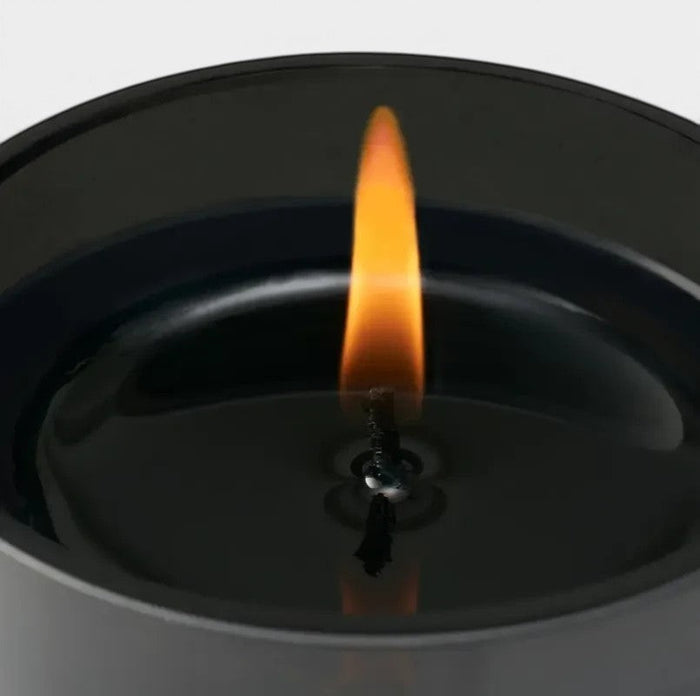 Shop Rescue Spa Coin Laundry candle in a black jar with a lit flame, featuring notes of aldehyde, pink pepper, rose, neroli, peony, violet, woods, musk, and sandalwood.