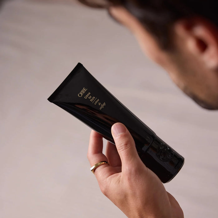 Shop Rescue Spa Oribe Creme for Style hair cream in a black squeeze tube held by a person with a gold ring.