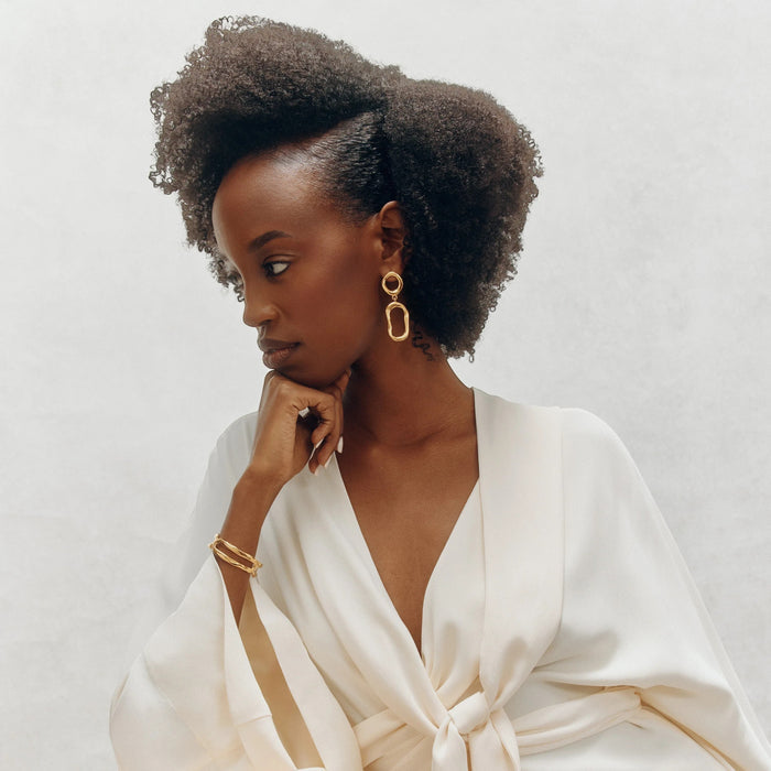 Shop Rescue Spa woman with defined natural curls wearing a white robe and gold jewelry, showcasing hair product.