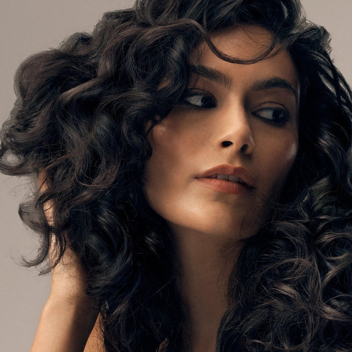 Shop Rescue Spa Curl Shaping Mousse on dark, wavy hair, adding definition and shine.
