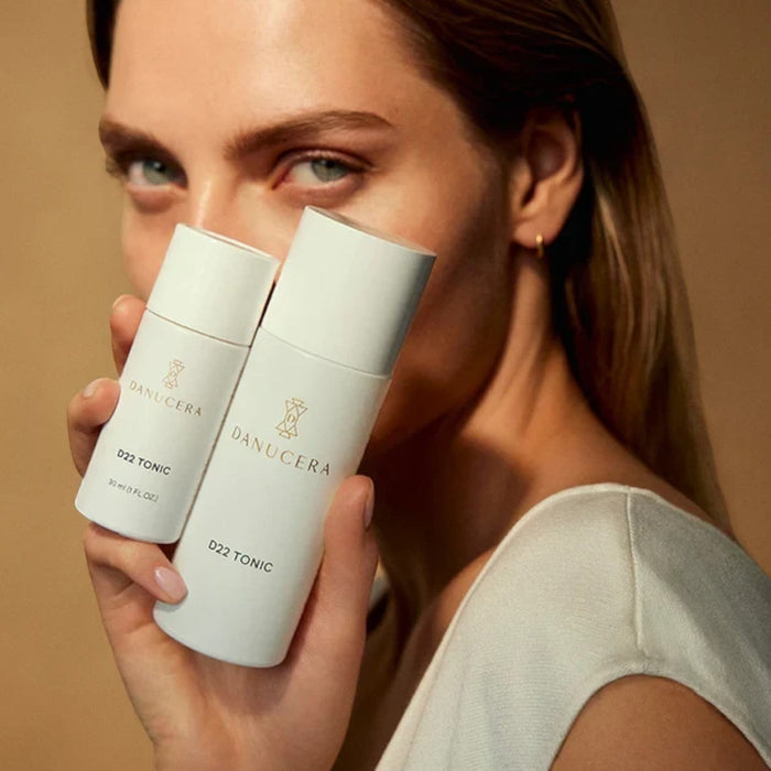 A woman holding two white Danucera D22 Tonic bottles from Shop Rescue Spa, featuring exfoliating facial toner.