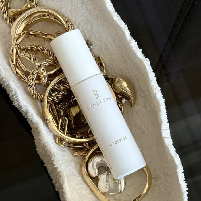 Shop Rescue Spa D7 Serum in a white bottle resting on a textured white dish surrounded by gold jewelry.