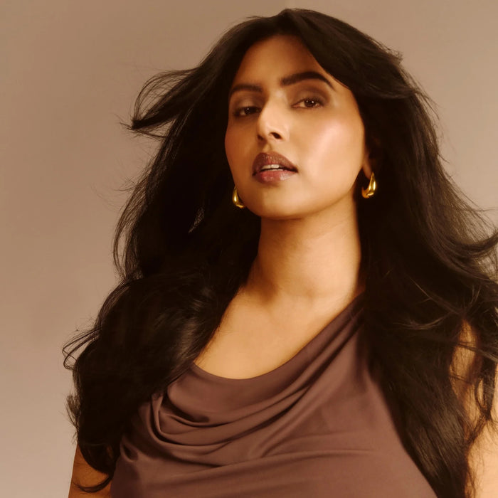 Shop Rescue Spa Dry Texturizing Spray model with voluminous, textured dark hair and a brown cowl-neck top
