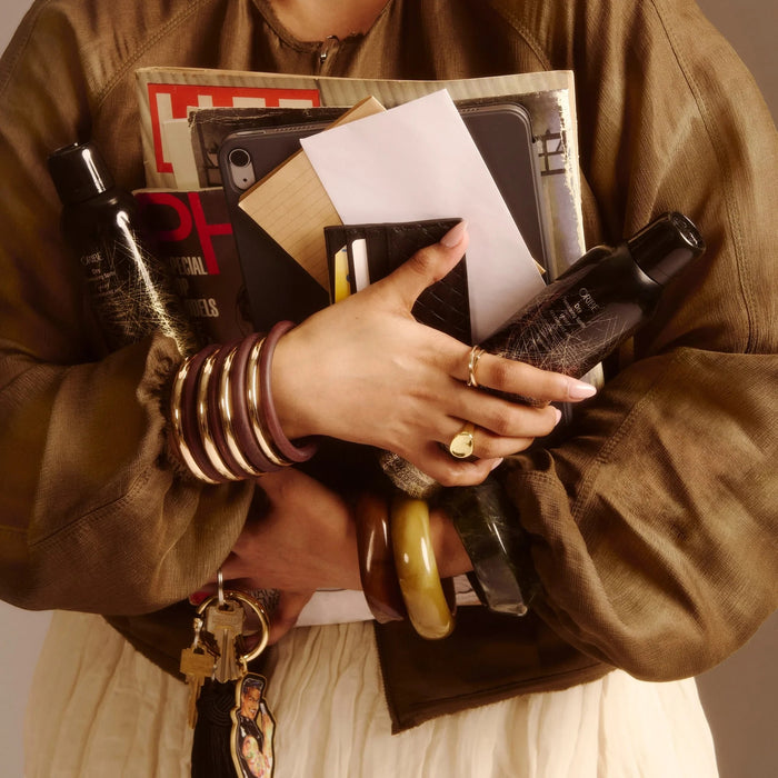 Shop Rescue Spa Dry Texturizing Spray bottles held by a person carrying magazines, a tablet, and a wallet.