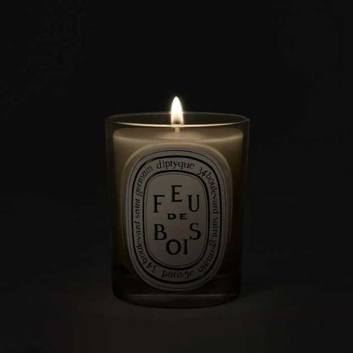 Shop Rescue Spa Diptyque Feu de Bois scented candle in a glass vessel with a glowing flame against a dark background.