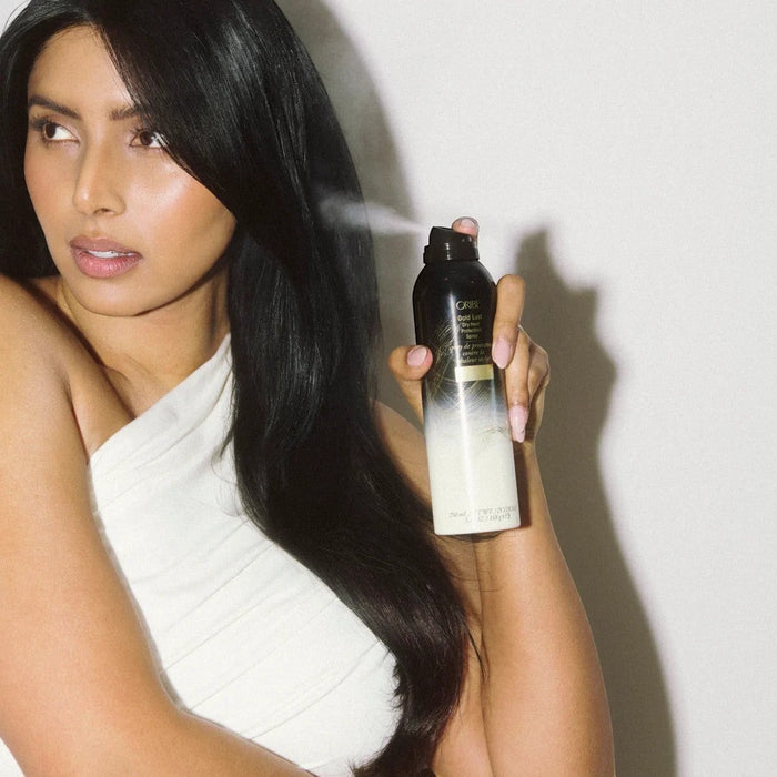 Shop Rescue Spa model with long dark hair spraying Oribe Gold Lust Dry Heat Protection Spray, protecting hair from heat.