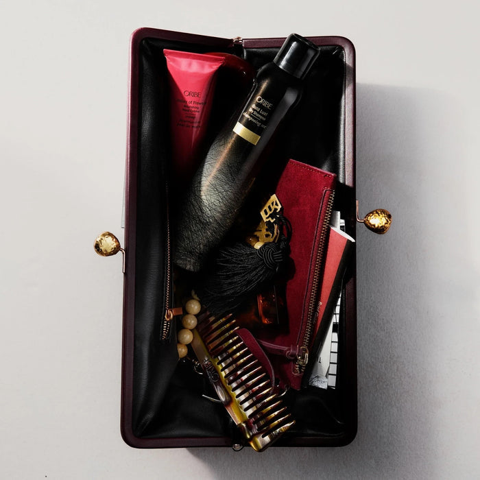 Shop Rescue Spa Oribe Gold Lust dry shampoo inside a dark burgundy clutch with a comb and beauty products