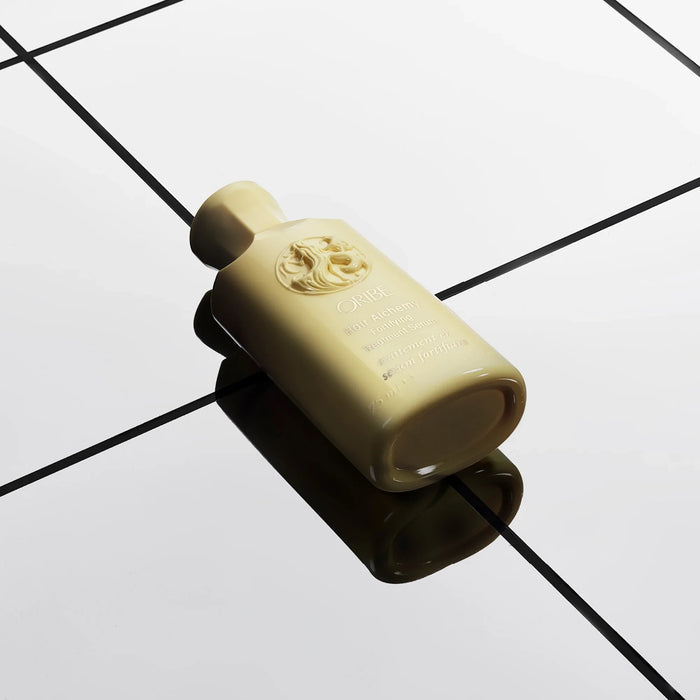 Shop Rescue Spa Oribe Hair Alchemy Fortifying Treatment Serum in a pale yellow bottle on a reflective grid surface.