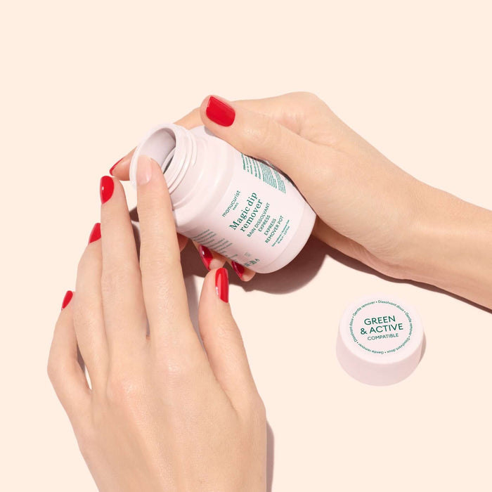 A person's hands with red nail polish hold an open white jar of makeup cream against a pale beige background, with the lid placed beside it. The jar label reads 'Makeup Cream' and 'GREEN & ACTIVE'.