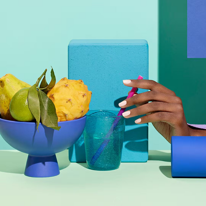 Shop Rescue Spa Manucurist Green Flash gel polish in a soft neutral shade on a model's hand next to fruit and decor.
