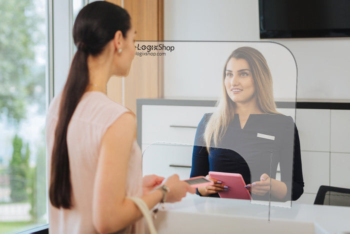 Reception desk with plexiglass shield divider and two women interacting in office setting