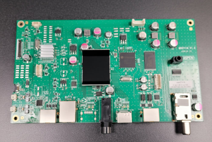 Green electronic circuit board with various components on a gray background