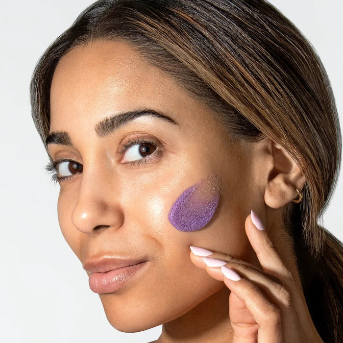 Shop Rescue Spa ReSURFACE Skin Polish applied as a purple exfoliating cream on a woman's cheek