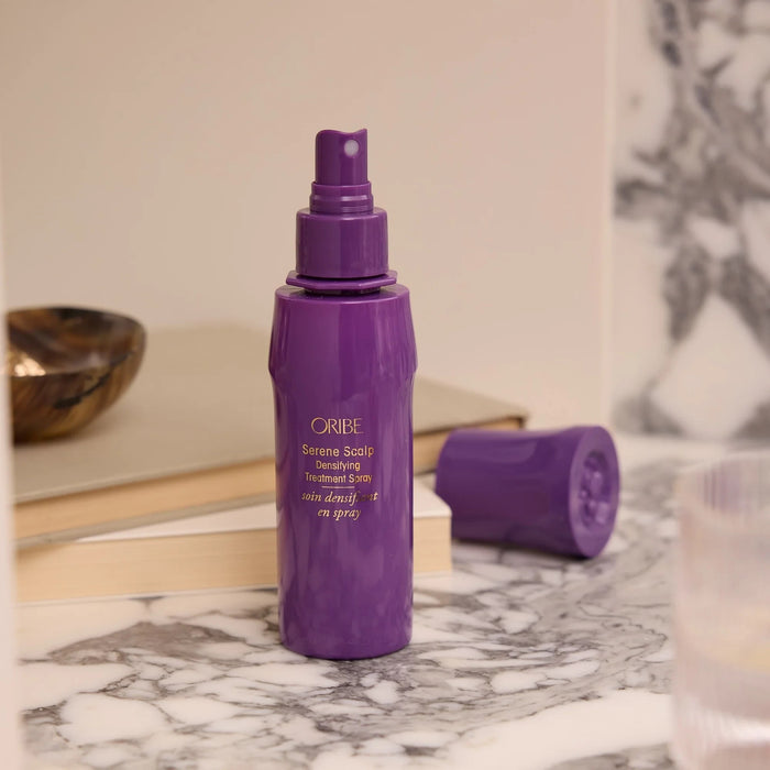 Shop Rescue Spa Oribe Serene Scalp Densifying Treatment Spray in a purple bottle on a marble countertop.