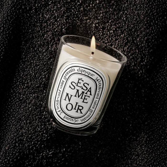 Shop Rescue Spa Sesame Noir scented candle in a glass vessel, surrounded by a bed of roasted black sesame seeds.