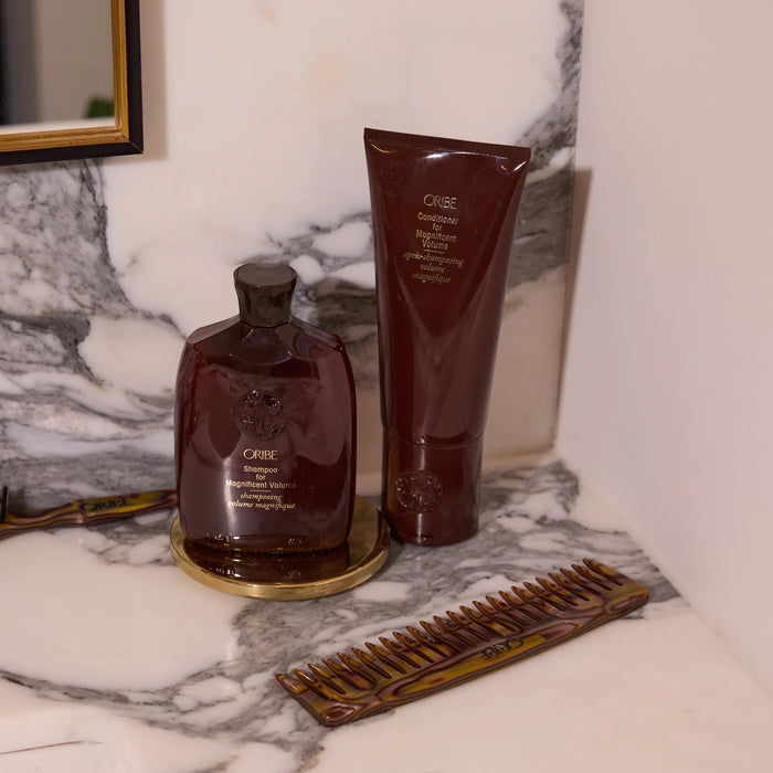 Shop Rescue Spa Oribe Shampoo and Conditioner for Magnificent Volume set with a tortoiseshell comb on marble vanity