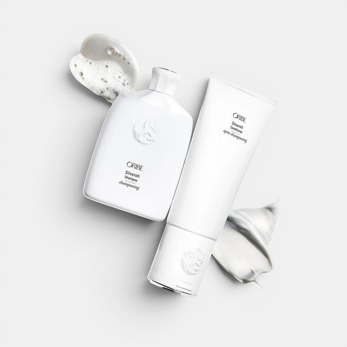 Oribe Silverati Shampoo and Conditioner bottles with white foam and cream on a white background.