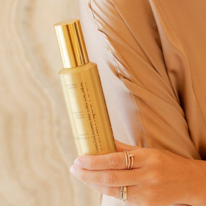 Shop Rescue Spa Sublime Gold leave-in hair treatment shield in a gold bottle held by a woman in a silk top.