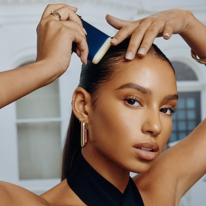 Shop Rescue Spa Supershine Smoothing Wax Stick tames flyaways and adds shine to styled hair. Model applies wax to hairline.