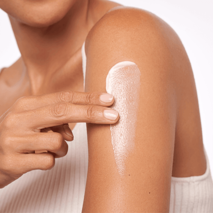 Person applying a white cream or lotion to their arm on a plain background