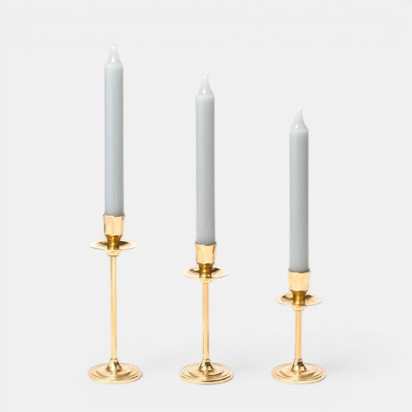 Trudon gold-plated candlestick trio with Madeleine taper candles, arranged smallest to tallest on a grey background